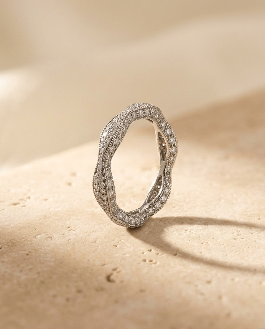 Éclat Ring by ALTUNA — macro three-quarter view of the pavé-set undulating eternity band on warm travertine