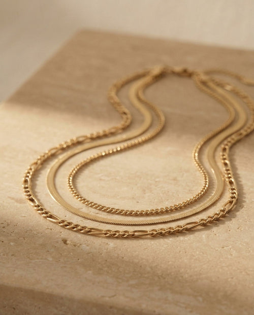 Camille Necklace by ALTUNA — angled studio view of the three-strand gold chain layering set on warm travertine