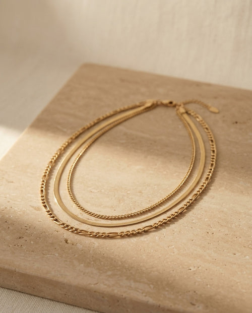 Camille Necklace editorial — layered gold chains on warm travertine