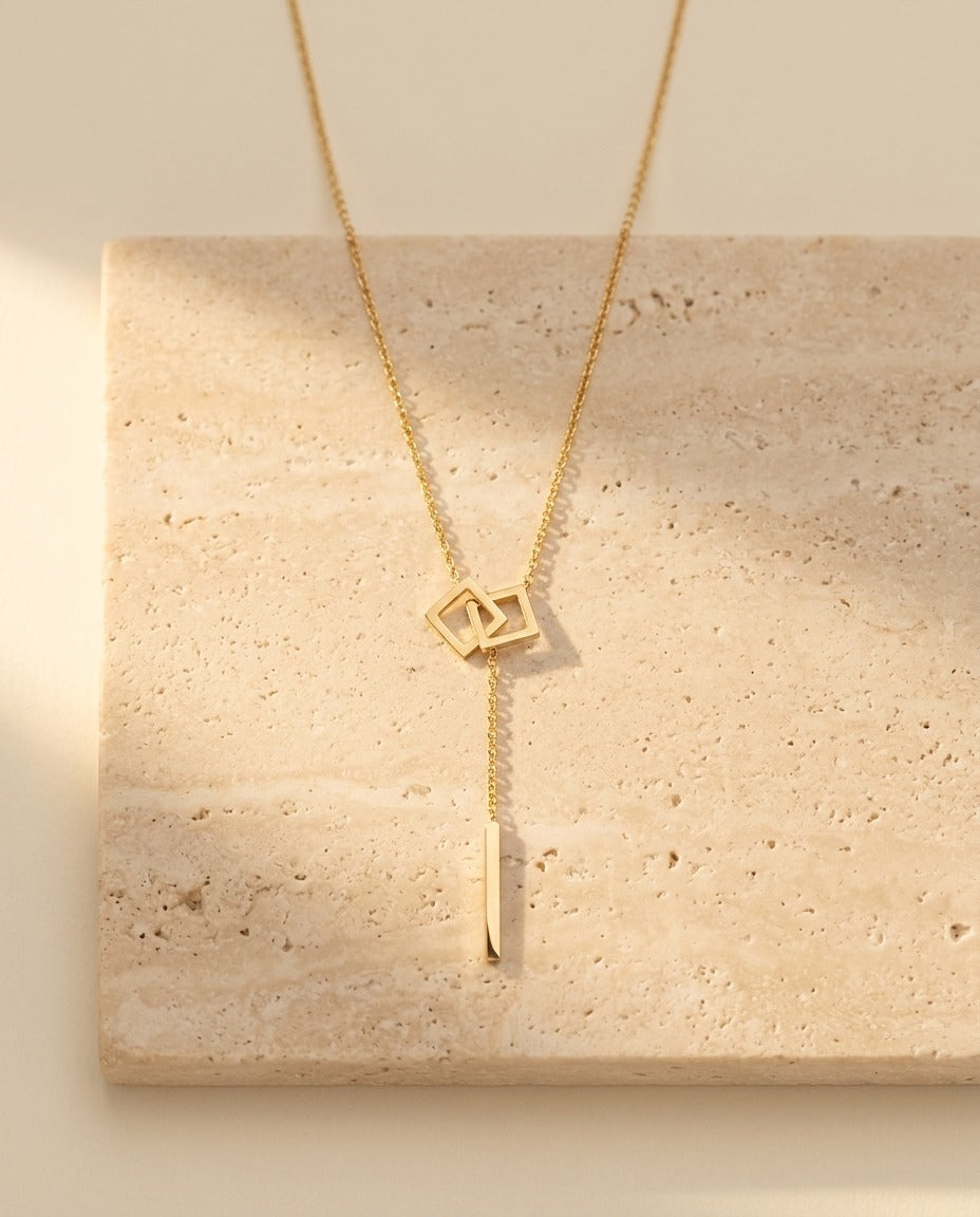 Carre Lumiere Necklace gold lariat with interlocking squares on travertine