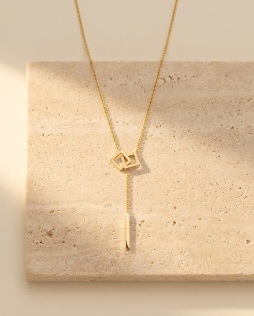 Carre Lumiere Necklace gold lariat with interlocking squares on travertine