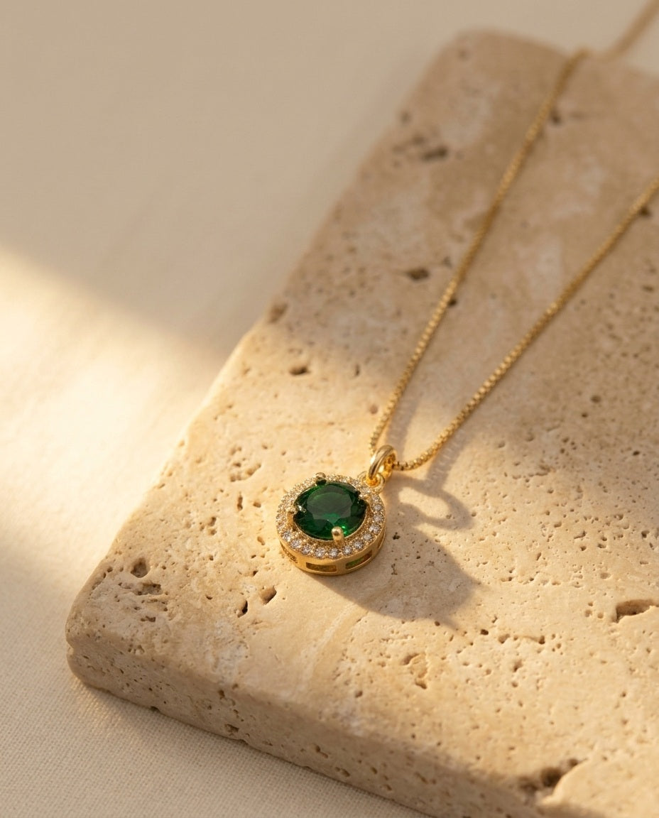 Celina Pendant Necklace in emerald, macro detail of the pavé halo and gold box chain on travertine