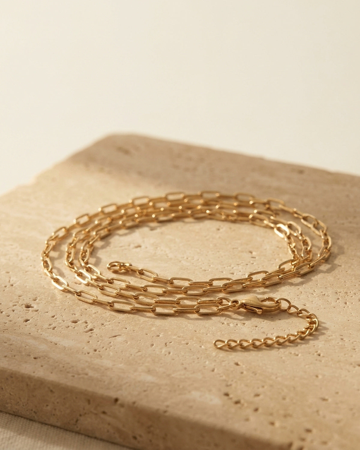 Céline Choker — macro detail of the fine yellow-gold paperclip chain and lobster clasp on warm travertine, ALTUNA