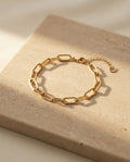 Doré Link Bracelet - gold paperclip link chain bracelet on warm beige travertine in soft sunlight