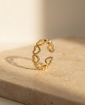 Endless Love Ring, gold open heart band, editorial still life on warm travertine