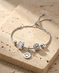 Love Charm Bracelet resting on warm beige travertine in soft golden light