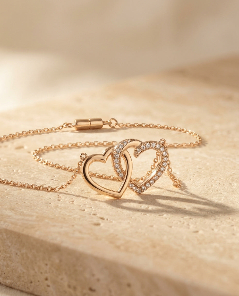 Lovebound Double Heart Necklace close detail angle, interlocking polished and pave gold hearts on warm beige travertine