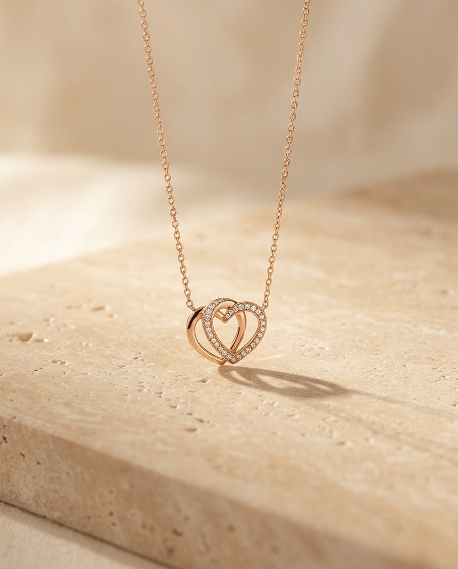 Lovebound Double Heart Necklace resting on warm beige travertine in soft golden light