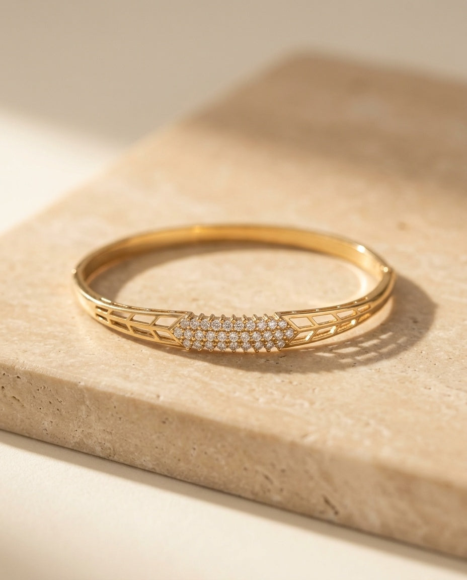 Lucia Bangle in yellow gold resting on warm travertine stone in soft sunlight