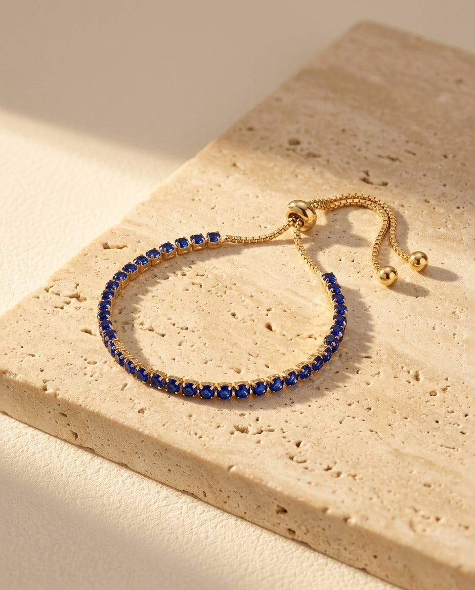 Seraphine Bracelet in Blue - yellow gold tennis bracelet with deep royal blue stones on warm travertine