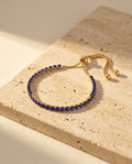 Seraphine Bracelet in Blue - yellow gold tennis bracelet with deep royal blue stones on warm travertine