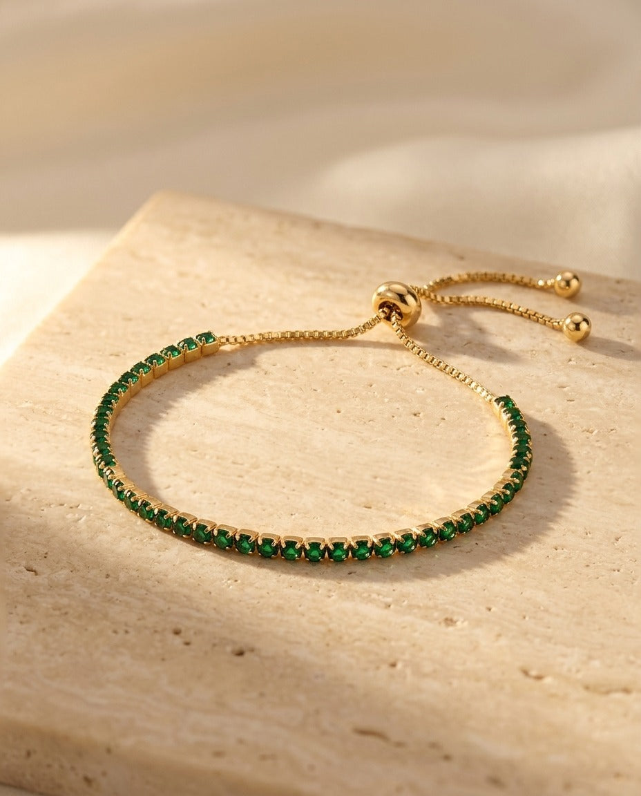 Seraphine Bracelet in Green - yellow gold tennis bracelet with deep green stones on warm travertine