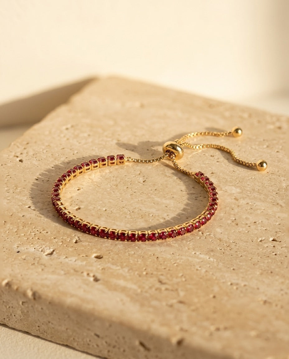 Seraphine Bracelet in Red - yellow gold tennis bracelet with deep red stones on warm travertine