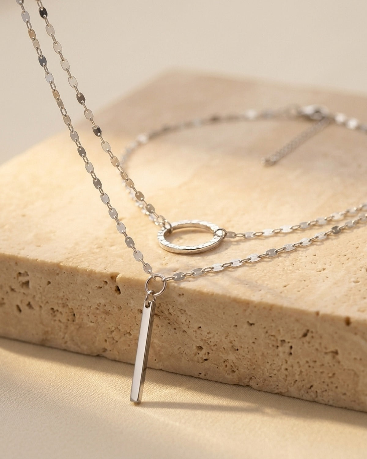 Sylara Necklace - silver double-layered lariat with hammered open circle and bar drop, detail angle on travertine