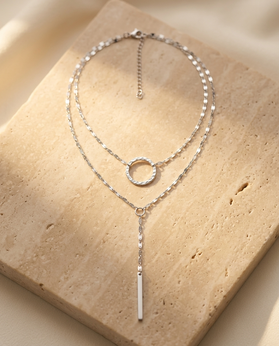 Sylara Necklace editorial - silver layered lariat on warm beige travertine