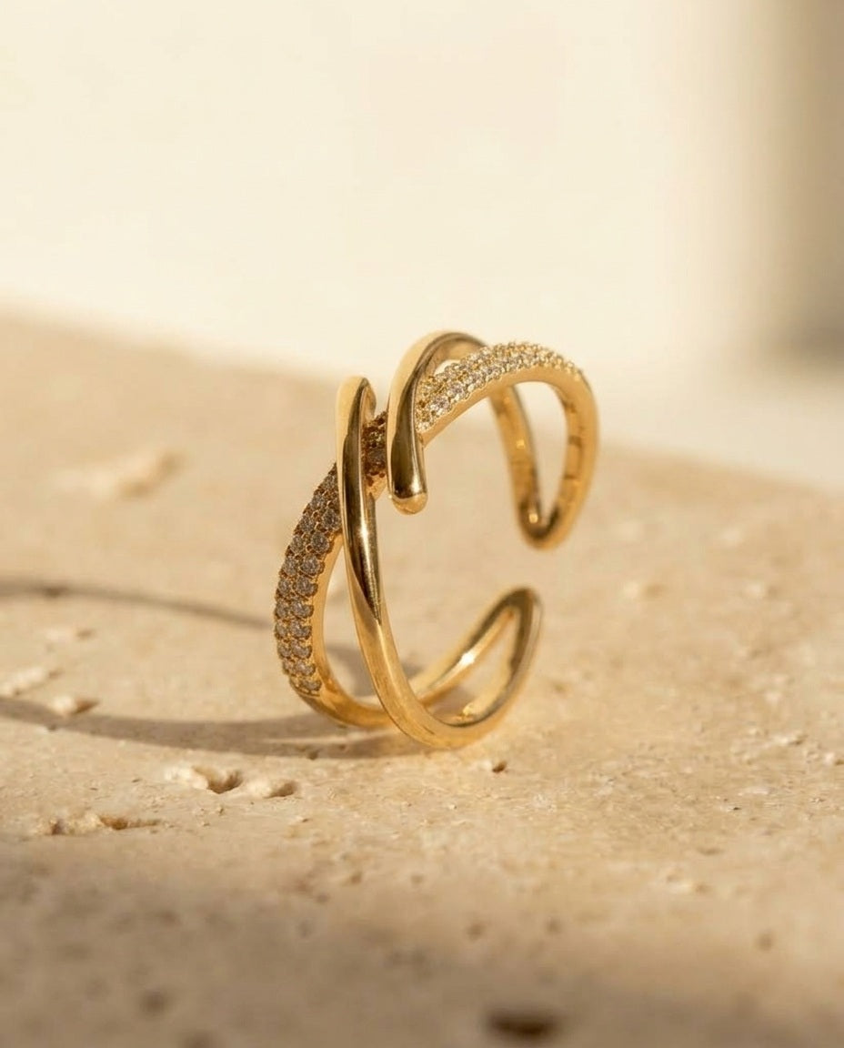 ALTUNA Sync Ring in gold - macro three-quarter detail of the open crossover bands on travertine