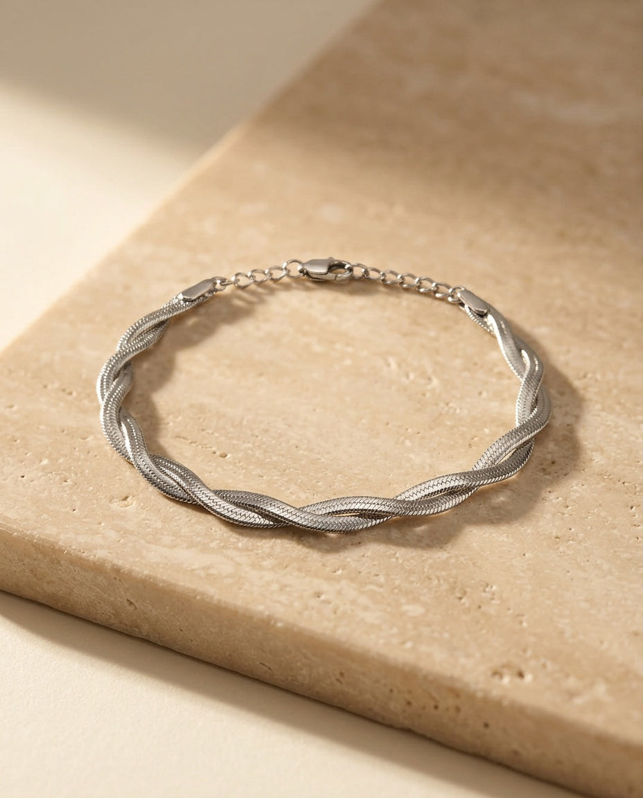 Twisté Bracelet in polished silver, twisted herringbone strands, resting on warm beige travertine