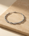 Twisté Bracelet in polished silver, twisted herringbone strands, resting on warm beige travertine