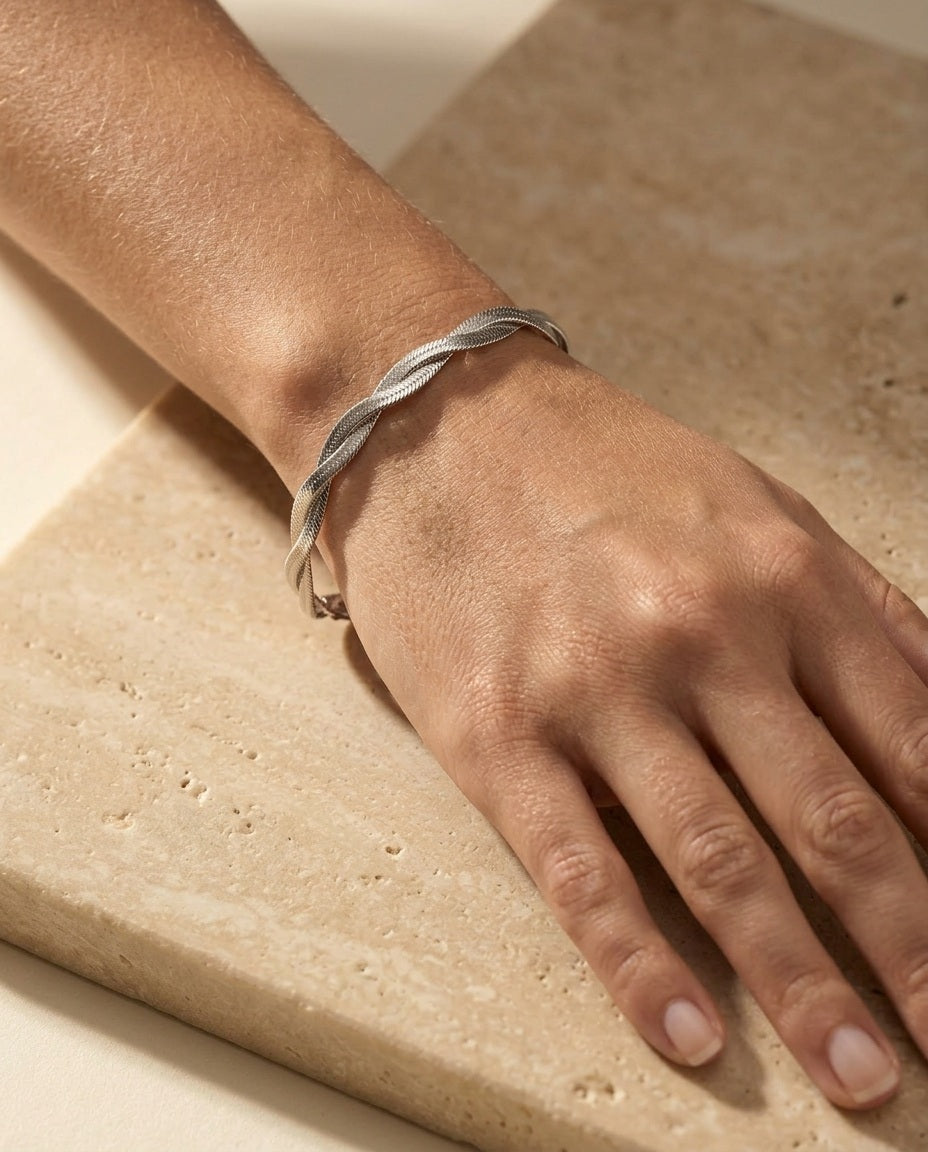 Twisté Bracelet worn on a woman's wrist, polished silver braided herringbone twist, warm natural light on travertine